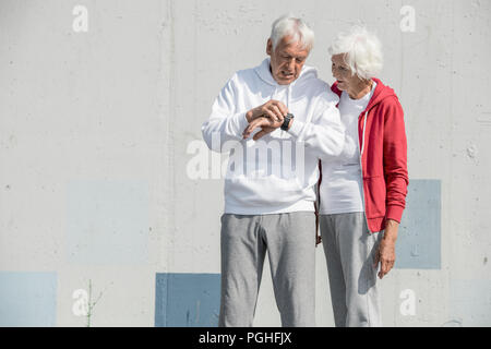 Waist up portrait of modern senior couple setting up smart watch and listening to music while doing morning run in park, copy space Stock Photo