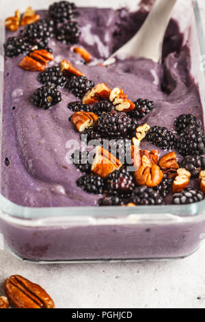 Homemade berry ice cream in a glass container. Vegan blackberry ice cream with pecan and coconut cream. Stock Photo