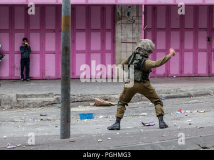 Hebron, Palestine, November 29, 2013: Israel Defence Forces soldier is throwing a gas grenade to disperse Palestinian young man during riots in Hebron Stock Photo