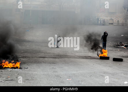 Hebron, Palestine, November 29, 2013:  Palestinian woman walks the street while young man is lifting his feast in sign of disapproval towards Israeli  Stock Photo