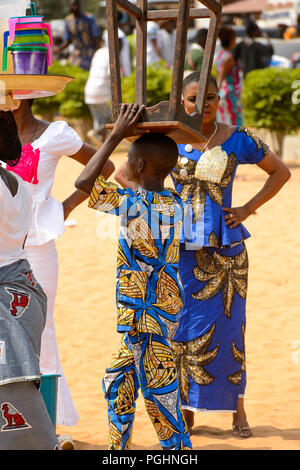 OUIDAH, BENIN - Jan 10, 2017: Unidentified Beninese  little boy in colored suit carries a wooden chair on his head at the voodoo festival, which is an Stock Photo