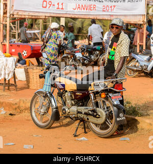 OUIDAH, BENIN - Jan 10, 2017: Unidentified Beninese man stands near his motorcycle at the local market. Benin people suffer of poverty due to the bad  Stock Photo