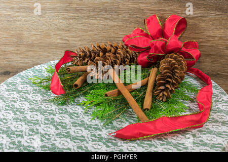 Three white pine cones on a bed of cedar and balsam branched, with six gold twig balls, three red ornaments, and five cinnamon sticks Stock Photo
