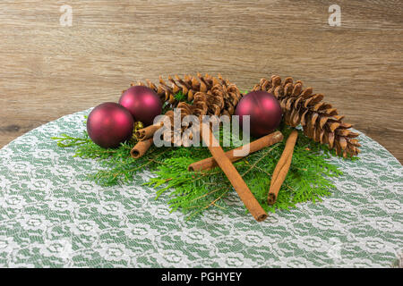 Three white pine cones on a bed of cedar and balsam branched, with six gold twig balls, three red ornaments, and five cinnamon sticks Stock Photo