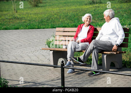 Full length portrait of loving senior couple chatting happily sitting on bench enjoying windy autumn day in park, copy space Stock Photo