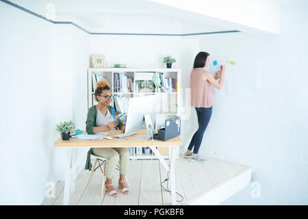 Full length portrait of two modern designers working in small white office, focus on African-American woman sitting at desk, copy space Stock Photo