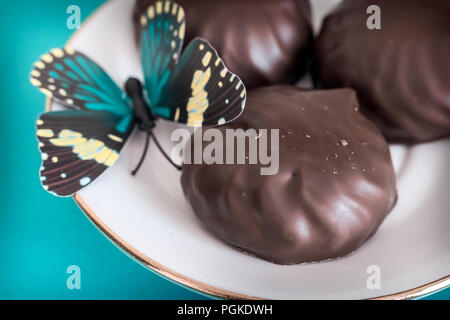 On a green background on a plate of marshmallows covered with chocolate. Next decoration in the form of an artificial butterfly. Stock Photo