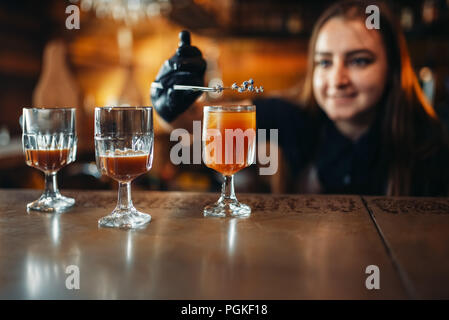 Female bartender prepares alcoholic coctail. Alcohol drink preparation. Barman working at the bar counter in pub Stock Photo