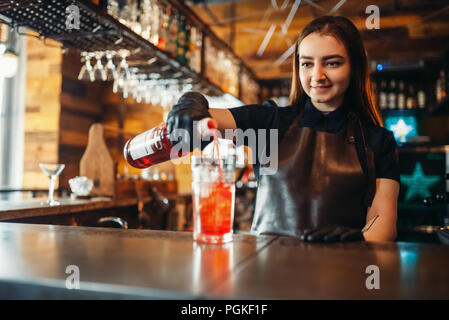 Female barman prepares alcoholic coctail with ice. Alcohol drink preparation. Woman bartender working at the bar counter in pub Stock Photo