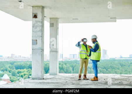 Full length portrait of two contemporary workers using VR to visualize projects standing in unfinished building on construction site, copy space Stock Photo