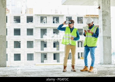 Full length portrait of two contemporary crew workers using VR to visualize projects standing in unfinished building on construction site, copy space Stock Photo