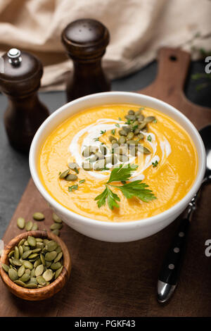 Pumpkin cream soup with cream, pumpkin seeds in bowl on wooden serving board. Closeup view, selective focus Stock Photo