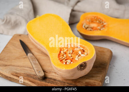 Butternut pumpkin cut in half on wooden cutting board. Preparation of pumpkin pie, pumpkin soup. Autumn comfort food cooking Stock Photo