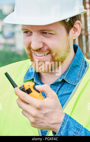 Head and shoulders portrait of bearded construction foreman speaking by walkie-talkie giving instructions to workers on site Stock Photo