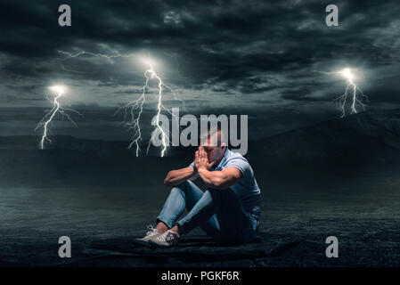 Young man sitting on the ground in desert, storm with lightning flash on background Stock Photo