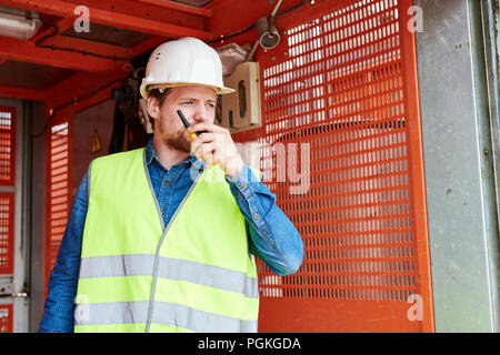Waist up portrait of construction worker standing in elevator and speaking by walkie-talkie giving instructions to crew on site, copy space Stock Photo