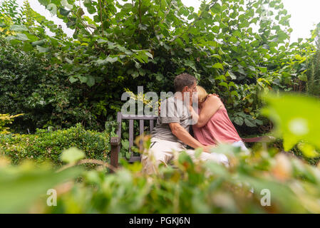 Couple kissing while sitting on a bench in a park garden. Stock Photo