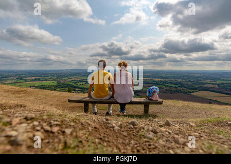 Couple sitting on a bench in the Malvern Hills, Worcestershire looking into the distance and overlooking the English countryside on a sunny summer day Stock Photo