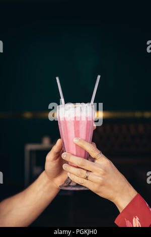 Close up of hands of a couple holding a glass of milkshake with two straws. Stock Photo