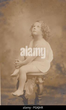 Vintage Photograph of a Blond Curly Haired Boy Child Sat on a Pedestal Wearing a Toga (Cherub Image) Stock Photo