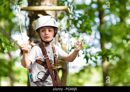 Happy kid climbing on high wire in a adventure park Stock Photo