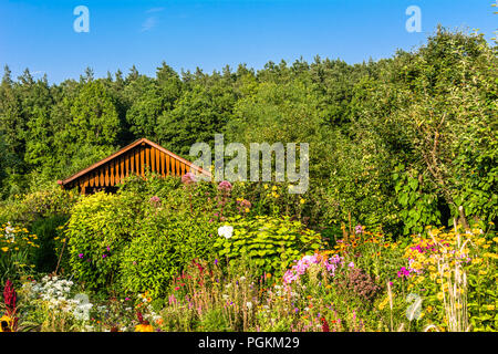 Wooden cottage in garden scenery with a small garden house, flowers and trees Stock Photo