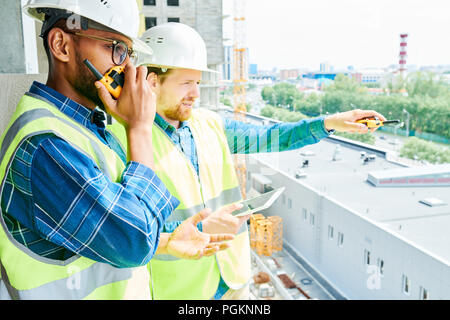 Side view  portrait of two construction workers wearing hardhats and reflective vests working on site Stock Photo
