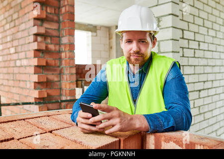 Portrait of bearded construction worker smiling at camera while leaning on brick wall on site, copy space Stock Photo