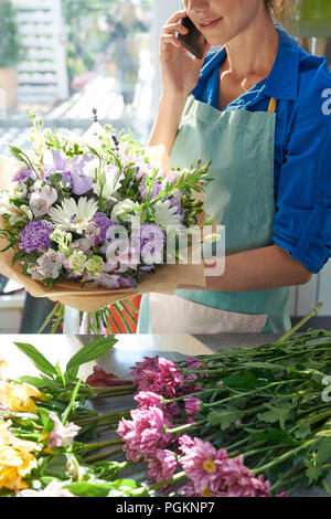 Crop view of unrecognizable florist speaking by phone while arranging flowers in shop Stock Photo