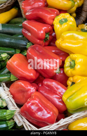 a selection of fresh red, green and yellow peppers with courgettes on sale at a market stall in a colourful display/ Stock Photo