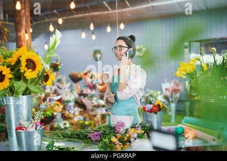 Side view portrait of young woman speaking by phone in flower shop Stock Photo