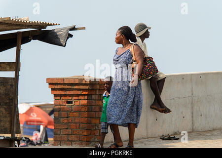 ELMINA, GHANA -JAN 18, 2017: Unidentified  Ghanaian woman walks with her child along the coast of Elmina. People of Ghana suffer of poverty due to the Stock Photo