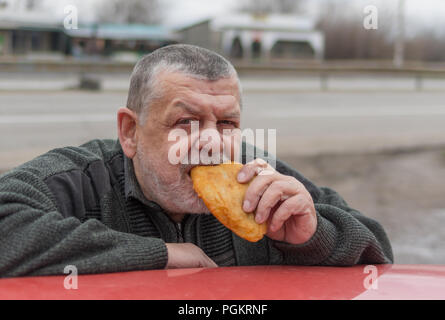 Hungry senior driver eating patty leaning his elbows on the car roof Stock Photo