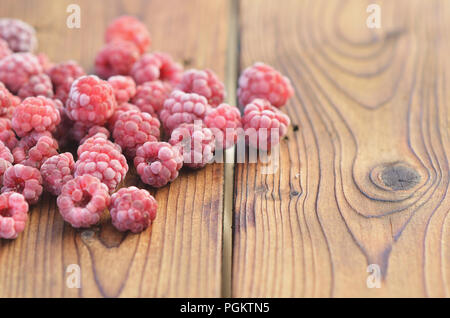 Raspberries covered with frost lie on a wooden background on the left side Stock Photo