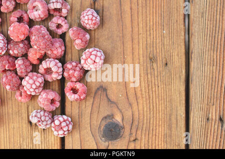 Raspberries covered with frost lie on a wooden background on the left side, a photo from above Stock Photo