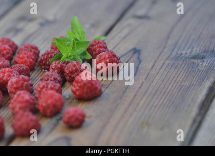 Late raspberry berries are covered with frost, lie on a wooden background, among them a sprig of green fresh mint Stock Photo