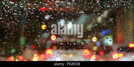 Blurred vehicle tail lamps viewed through water droplets on car windshield Stock Photo