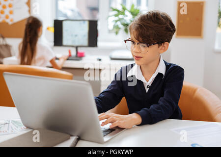 Smart boy using a laptop in a classroom Stock Photo