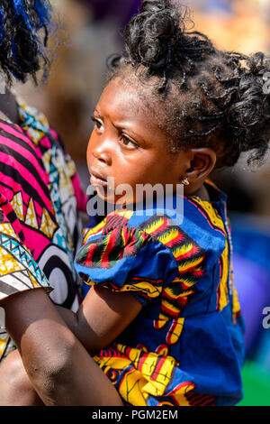 BOHICON, BENIN - JAN 12, 2017: Unidentified Beninese beautiful little girl is carried by her mother at the local market. Benin children suffer of pove Stock Photo