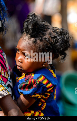 BOHICON, BENIN - JAN 12, 2017: Unidentified Beninese beautiful little girl is carried by her mother at the local market. Benin children suffer of pove Stock Photo