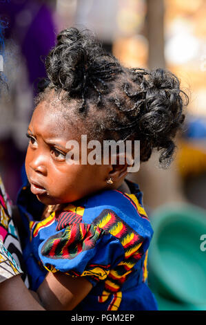 BOHICON, BENIN - JAN 12, 2017: Unidentified Beninese beautiful little girl is carried by her mother at the local market. Benin children suffer of pove Stock Photo