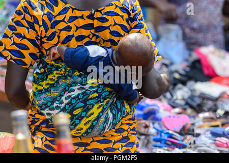 BOHICON, BENIN - JAN 12, 2017: Unidentified Beninese little baby is carried by his mother at the local market. Benin children suffer of poverty due to Stock Photo