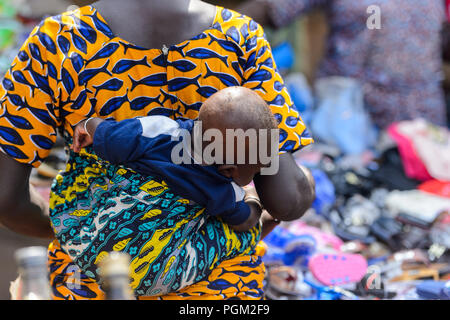 BOHICON, BENIN - JAN 12, 2017: Unidentified Beninese little baby is carried by his mother at the local market. Benin children suffer of poverty due to Stock Photo