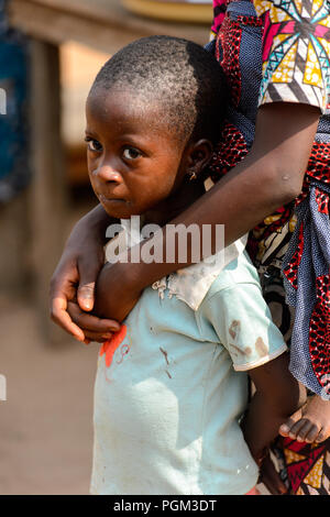 BOHICON, BENIN - JAN 12, 2017: Unidentified Beninese little girl is hugged by her mother at the local market. Benin children suffer of poverty due to  Stock Photo