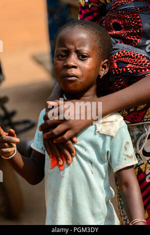 BOHICON, BENIN - JAN 12, 2017: Unidentified Beninese little girl is hugged by her mother at the local market. Benin children suffer of poverty due to  Stock Photo