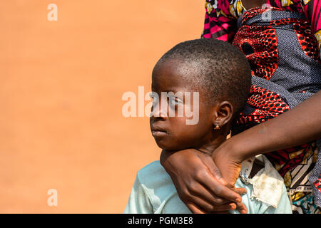 BOHICON, BENIN - JAN 12, 2017: Unidentified Beninese little girl is hugged by her mother at the local market. Benin children suffer of poverty due to  Stock Photo