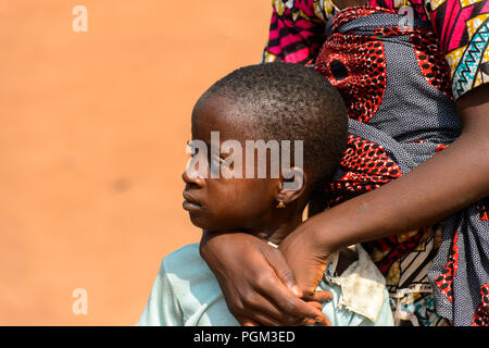 BOHICON, BENIN - JAN 12, 2017: Unidentified Beninese little girl is hugged by her mother at the local market. Benin children suffer of poverty due to  Stock Photo