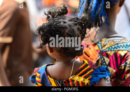 BOHICON, BENIN - JAN 12, 2017: Unidentified Beninese little curly girl is carried by her mother at the local market. Benin children suffer of poverty  Stock Photo