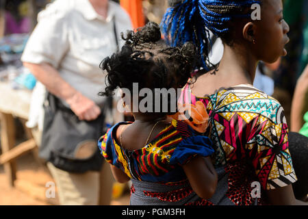 BOHICON, BENIN - JAN 12, 2017: Unidentified Beninese little curly girl is carried by her mother at the local market. Benin children suffer of poverty  Stock Photo