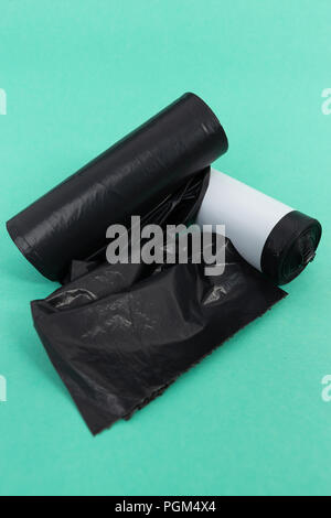 Black plastic garbage junk litter bag rolls as single use pollution household cleaning waste concept isolated on green background Stock Photo